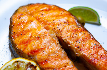 Salmon fish steak cooked on grill in seafood restaurant and sered on white plate with lemons
