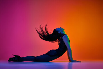 Wave movement. Young woman dancing contemp over gradient pink orange studio background in neon light. Concept of contemporary dance style, art, aesthetics, hobby, creative lifestyle