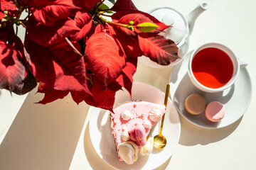 Pink cake with macaroons with hot red tea and Poinsettia flower
