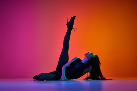 Passion and femininity. Young female dancer performing modern dance style over gradient pink orange studio background in neon light. Concept of contemporary dance style, art, aesthetics, creativity