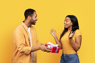 Smiling young african american guy give gift box to shocked woman, congratulate on holiday, anniversary