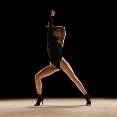 Self-expression. Attraction. Young woman in bodysuit and heels dancing, performing over black background. Concept of contemporary dance style, art, aesthetics, hobby, creative lifestyle