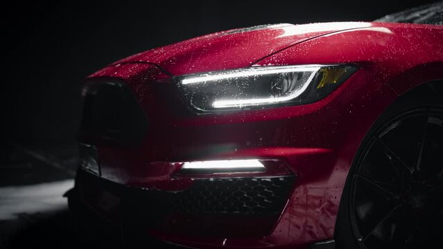 Close Up of a Modern Red Performance Car in a Dark Studio Environment. Creative Led Headlights Footage of a Performance Sportscar Dripping in Water After a Detailed Car Wash