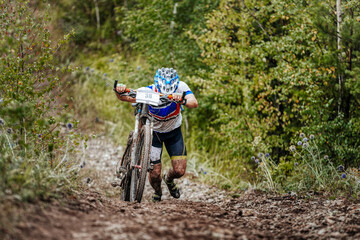 Fototapeta premium cyclist athlete with mountain bike walking uphill on forest trail