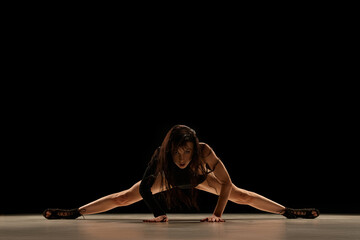 Fototapeta na wymiar On twine. Deep look. Young woman in bodysuit and heels dancing, performing over black background. Concept of contemporary dance style, art, aesthetics, hobby, creative lifestyle, flexibility