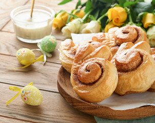 Naklejka na ściany i meble Easter breakfast Holliday concept. Easter bunny buns rolls with cinnamon made from yeast dough with orange glaze, easter decorations, colored eggs on old wooden background. Easter Holliday card.
