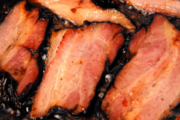 Frying Bacon Slices in a Pan. Crispy Pieces of Delicious Red Thin Smokey Bacon Fried in a Hot Skillet. Traditional Breakfast. Smoked Bacon Rasher or Strip Being Cooked. Grill. Fat High Calorie Food.