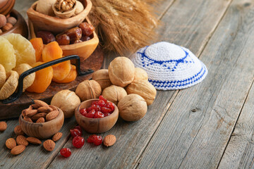 Fototapeta premium Tu Bishvat celebration concept. Mix of dry fruits and nuts almonds, hazelnuts, walnuts, apricots, prunes, cherries, raisins, dates, apples, figs over wooden table. Jewish holiday, new year of trees.