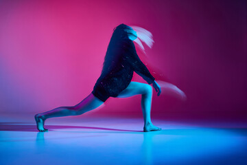 Young woman dancing contemp over gradient pink studio background in neon with mixed lights. Concept of contemporary dance style, art, aesthetics, hobby, creative lifestyle, flexibility