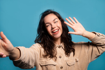 Happy pretty millennial european female student taking selfie and waving hand at camera