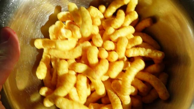 Some peanut flips chips are swayed inside the snack bowl . Chips snack in a silver bowl ready to eat . Unealthy but beautiful yummy food . Flying swayed peanut flips puffs concept footage .