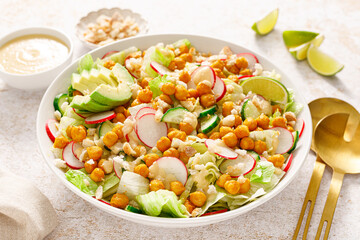 Healthy spring vegan Caesar salad with chickpea, fresh cucumber, radish, avocado and crispy croutons, dressed with garlic sauce.