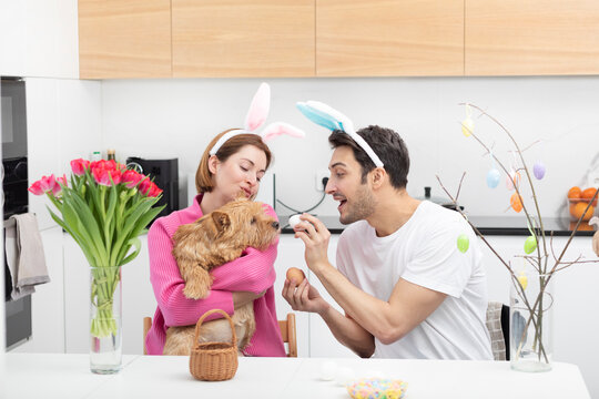Funny couple wearing bunny ears headband celebrating Easter together with their cute pet dog at home