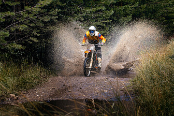 enduro racer riding on water with splashes motocross race in forest - obrazy, fototapety, plakaty