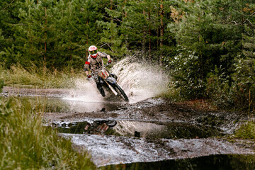motocross rider riding in puddle with splashes, forest enduro race