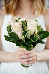 Obraz na płótnie Canvas Bride woman holds a wedding bouquet in her hands on the background of white dress. Wedding ceremony. Beautiful beige roses flower and green leaves. Tender sensual close up
