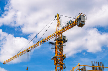 A tower construction crane on the background of a blue sky with clouds. Boom rotary crane with boom. Construction of apartment buildings in the city.