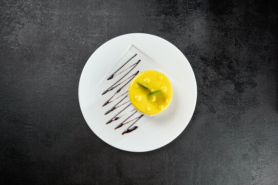 Mini Mango Cake On White Plate On Black Concrete Background. Mango Cheesecake In Minimal Style On Dark Backdrop. Light Dessert Of Cheese And Mango In Glaze Topped. Cheesecake With Tropical Flavour.