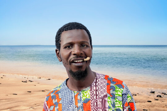 African man holding a miswak between his teeth at the beach (traditional teeth cleaning twig, also called sothio or sotio), photo