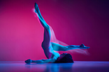 Dynamic portrait of young flexible woman dancing contemp, freestyle dance on gradient pink studio...