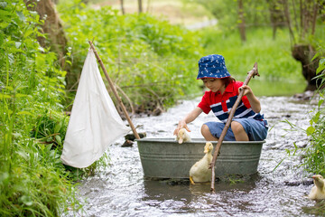 Cute child, boy, playing with boat and ducks on a little river