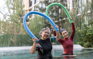 Young trainer helping senior woman in aqua aerobics and working out in the pool. old woman and...