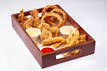wooden box with onion rings, crispy chicken, mozzarella sticks, fresh potatoes and sauces on isolated white background 