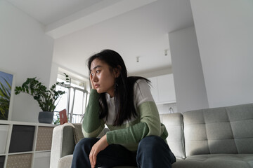 Unmotivated pensive Asian student girl sits on couch leaning head on hand. Procrastinating Chinese woman is stressed out because she doesnt want to start preparing for university entrance exams