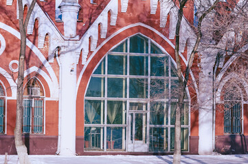 Facade of an old red brick building. Arched windows and white columns. Texture of frozen plants. Winter architectural landscape.