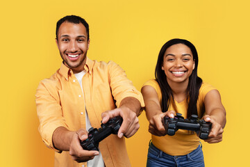 Happy young african american husband and wife with joystick have fun, playing computer online game