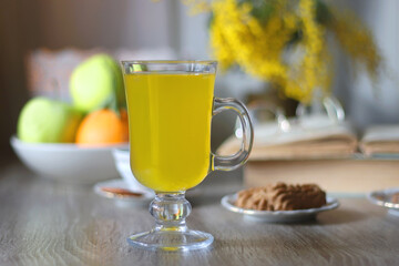 Cup of tea, plates with cookies, glass of orange juice, books, reading glasses, bowl of fruit and candles on the table. Selective focus.