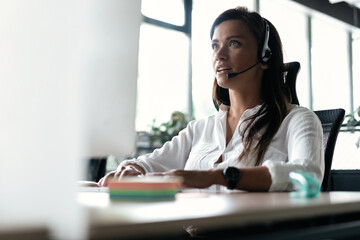 Friendly smiling woman call center operator with headset using computer at office.