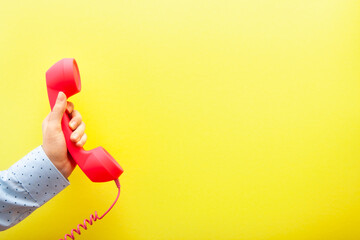 Communication and connection concept - woman hand with pink phone on yellow background with copy space
