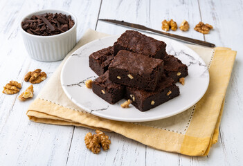Brownies on a plate with chocolate pieces and walnuts over white wooden table