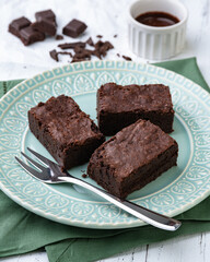 Brownies on a green plate with chocolate pieces and syrup over white wooden table