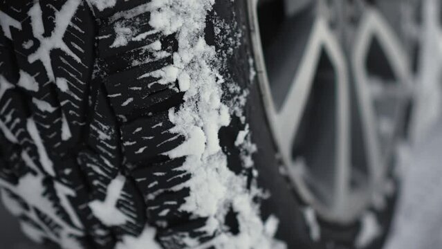 Car big wheels spin and spit up heavy wet snow as unknown driver tries to drive by snow country road with deep snowdrifts. SUV vehicle struggling to gain traction on winter road spews up snowy pieces