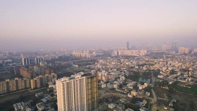 aerial drone shot curving from under construction building with crane and small buildings and houses in distance hidden in fog smog showing pollution from rapid growth in gurgaon