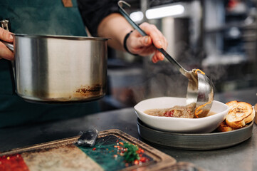 chef pouring tasty soup from pot into bowl on kitchen