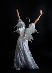 portrait of beautiful woman wearing  fantasy costume with white bridal gown  and translucent fairy wings.    Posing with gestural arms reaching out, isolated on black studio background.