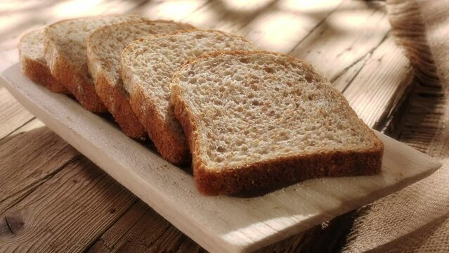 sliced bread on a wooden tray. breadboard on an old wooden table with cracks and rough fabric. baking in sun spots. rural lifestyle.