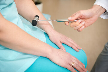 Pretty female orthopedist with patient in her office. Young doctor neurologist examining her patient with hammer. Neurologist checks the reflexes of a middle age female patient. Close up view.