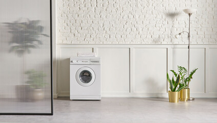 Washing machine in the bathroom, white brick wall background, vase of plant, cabinet and marble...