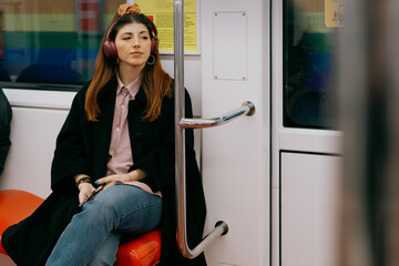 Portrait of a pensive young woman on the subway listening to music on headphones and waiting to go home