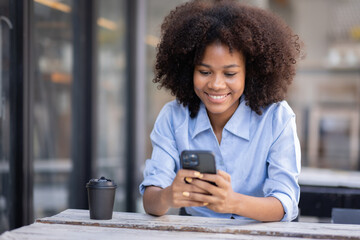 Smiling young woman sitting on chair holding mobile phone using cellphone device, looking at smartphone, checking modern apps, texting messages, browsing internet doing shopping relaxing at outside.
