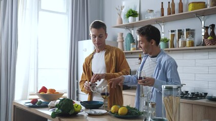 Stylish young adult male gay couple dancing at home in casual clothes in kitchen area. Handsome man preparing veggie lunch. Cute LGBTQ Relationship Content. High quality 4k footage - Powered by Adobe