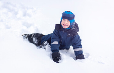 Fototapeta na wymiar A little boy lies in a snowdrift and smiles. Winter entertainment concept