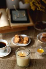 Scented candles, on the table. Selective focus.chocolate, cookies, cup of tea, books, e-reader, glasses and flowers on the table. Hygge at home. Selective focus.