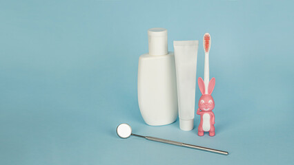 A set for children's oral hygiene: a toothbrush with a bunny, toothpaste, mouthwash and a dental mirror. The concept of dentistry and healthcare. Banner, blue background. Copy space for text