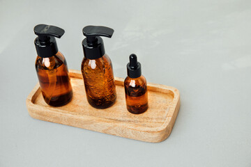 Amber bottles with facial cosmetics on a tray on the grey background. Top view