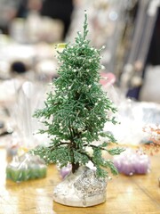 Small decorative tree bonsai made with green beads and wire on wooden table in shop window, closeup, selective focus